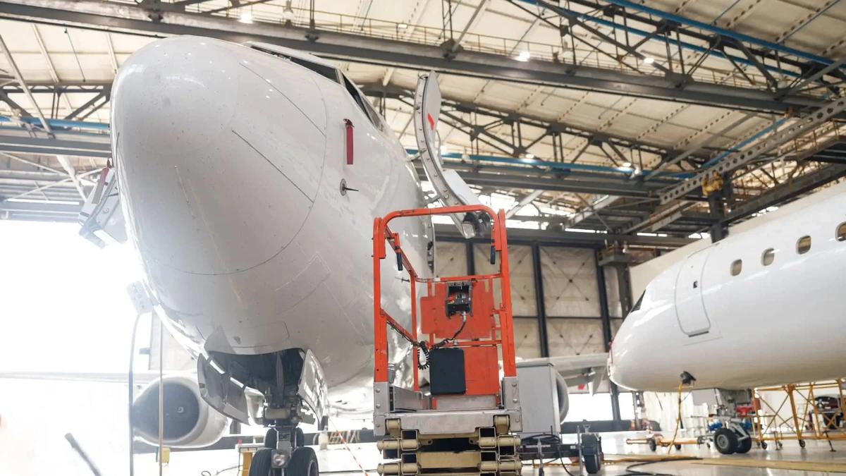 An aircraft undergoing maintenance inside a hangar, with technicians working on its hydraulic systems